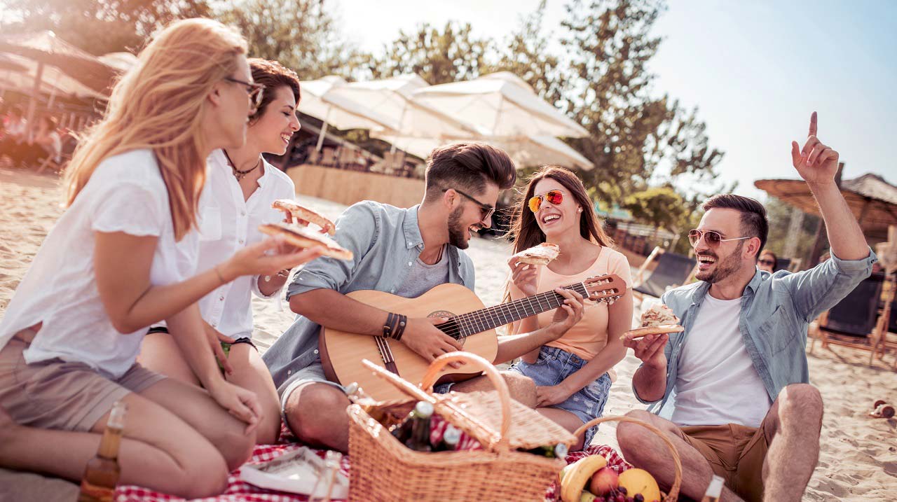 Gruppo di amici in spiaggia mangiano e suonano la chitarra