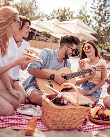 Gruppo di amici in spiaggia mangiano e suonano la chitarra