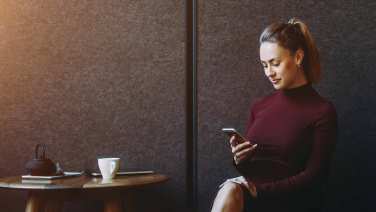 Giovane ragazza seduta in un caffè opera sul suo home banking da smartphone