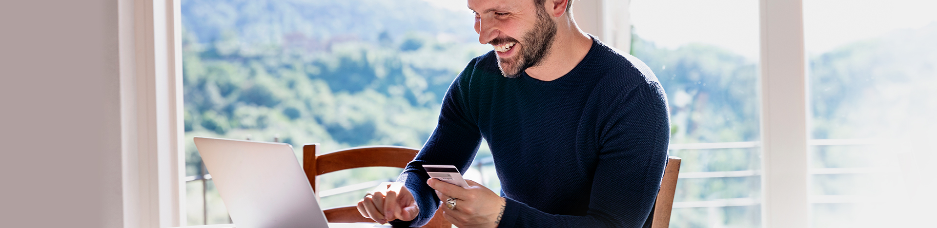 Uomo sorridente paga in sicurezza con la sua carta prepagata da laptop, comodamente dal proprio soggiorno.