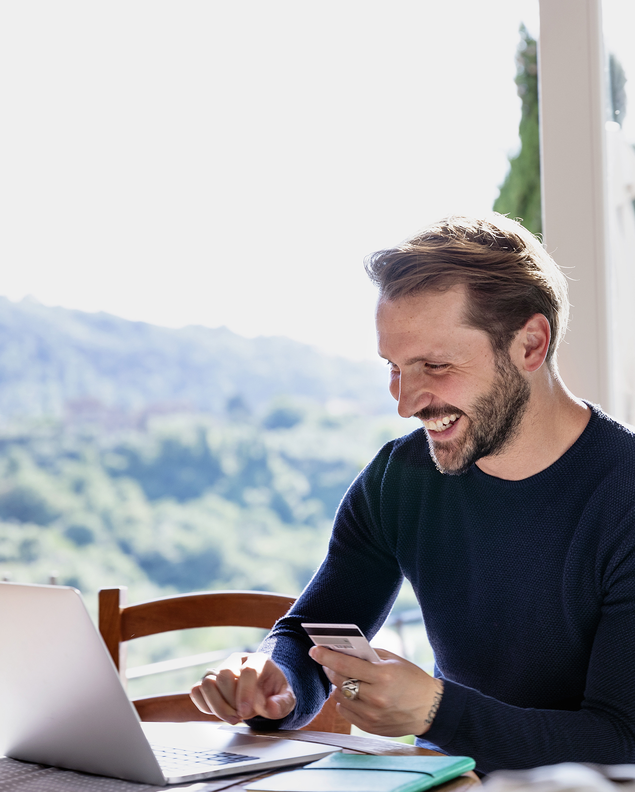 Uomo sorridente paga in sicurezza con la sua carta prepagata da laptop, comodamente dal proprio soggiorno.