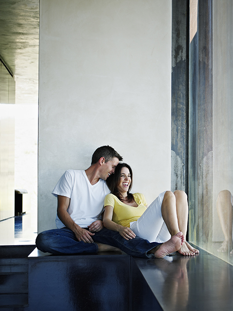 Marito e moglie siedono sorridenti vicino all'ampia finestra della loro casa di design.