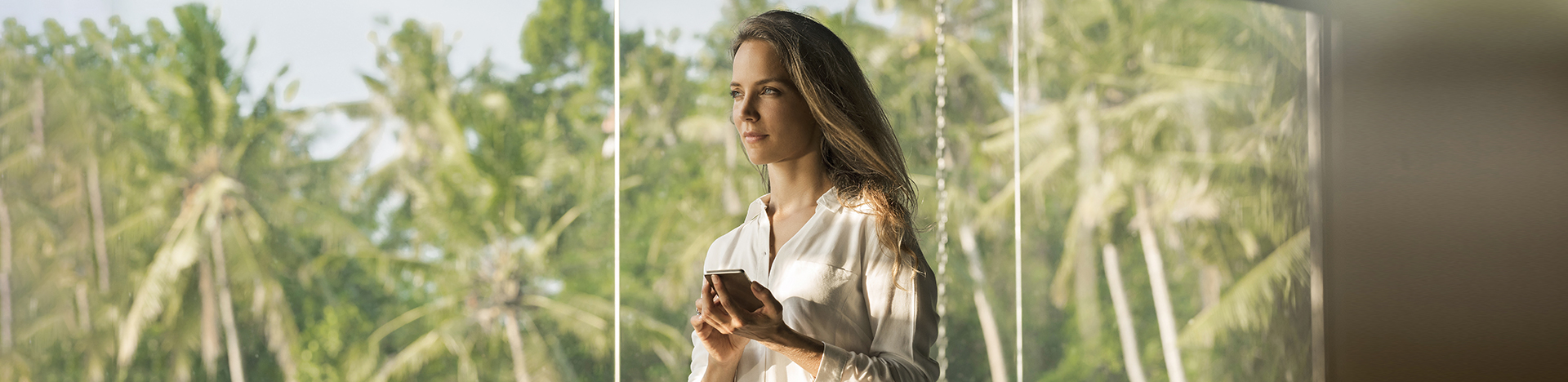 Donna dall'espressione serena opera con lo smartphone nella sua casa di design di fronte a un giardino lussureggiante.