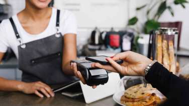 Giovane donna paga in un caffè con il proprio smartphone.