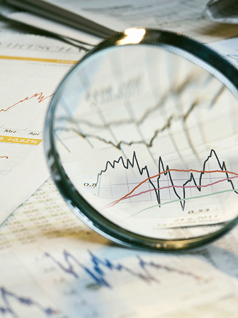 Lente di ingrandimento e giornali con tassi di cambio e diagrammi dei mercati finanziari.