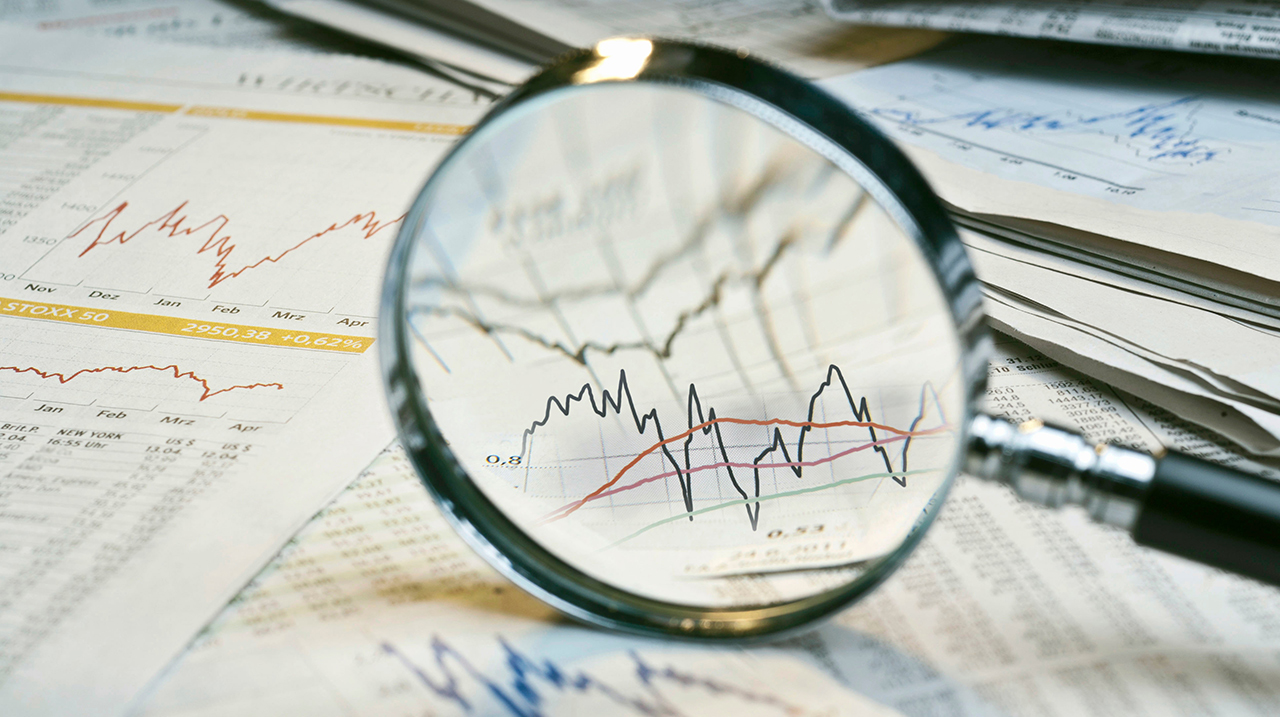 Lente di ingrandimento e giornali con tassi di cambio e diagrammi dei mercati finanziari.