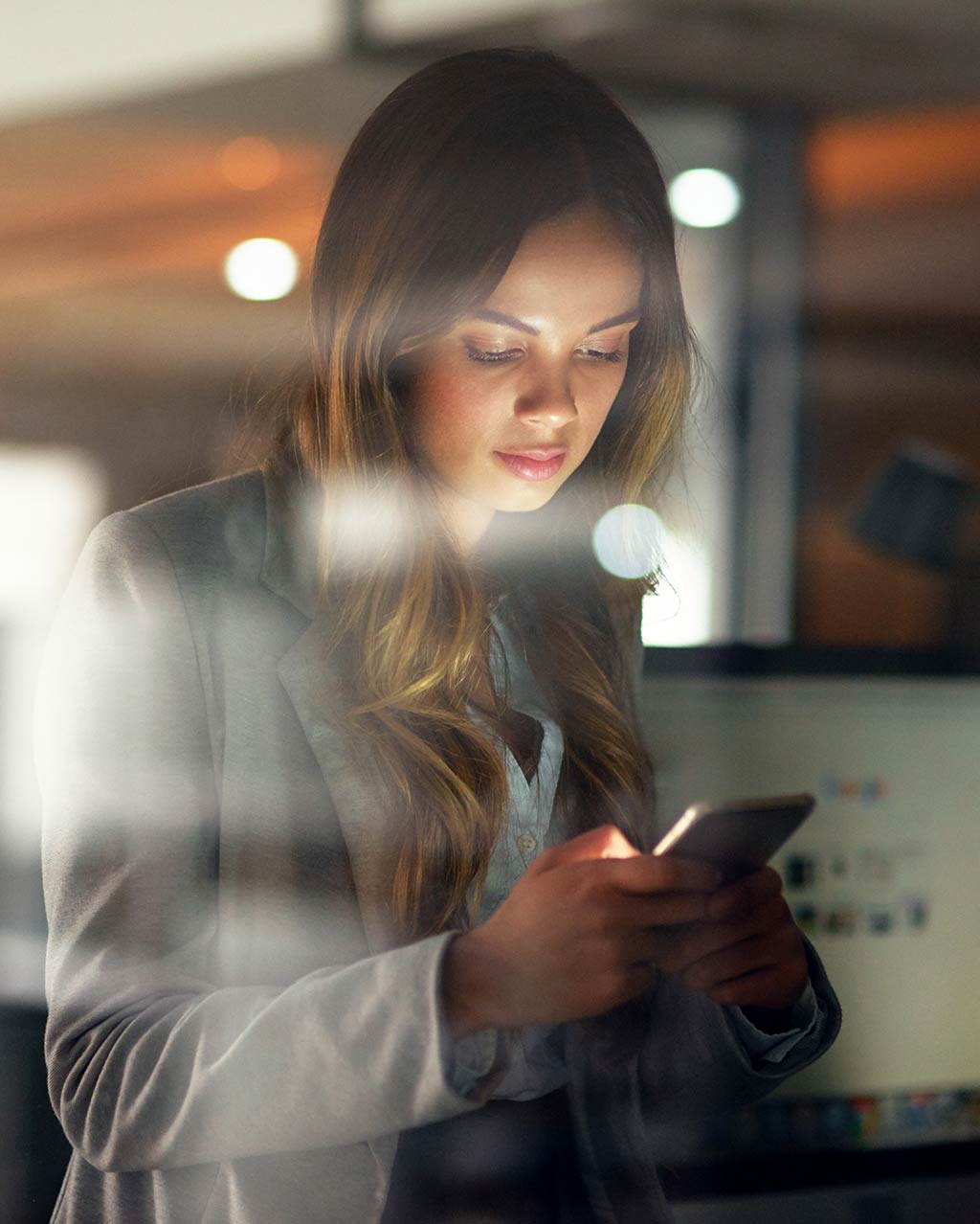 Donna accanto a scrivania legge sul suo smartphone​.