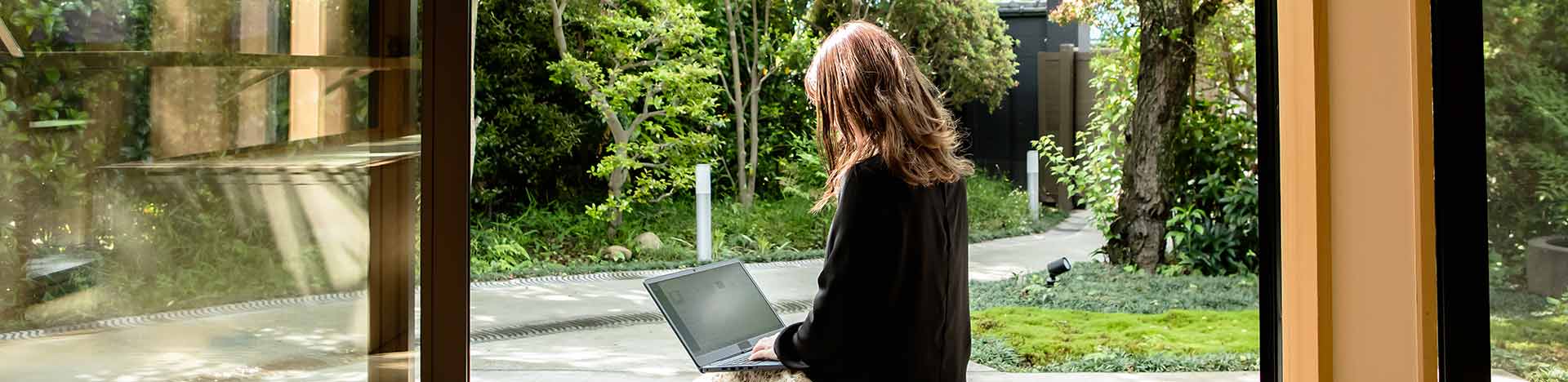 Donna lavora su laptop sotto un portico in giardino​.