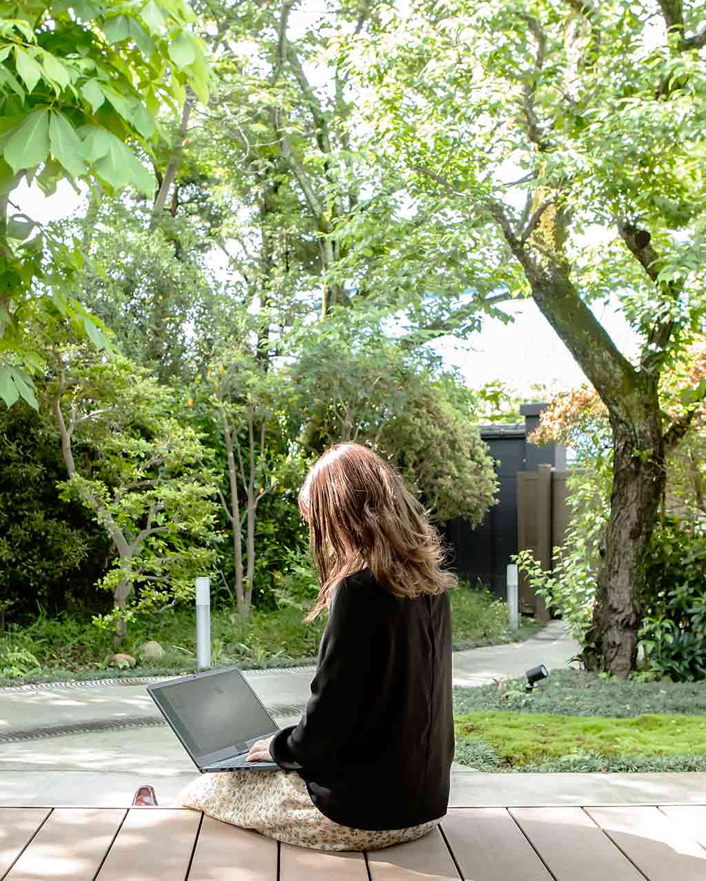 Donna lavora su laptop sotto un portico in giardino​.