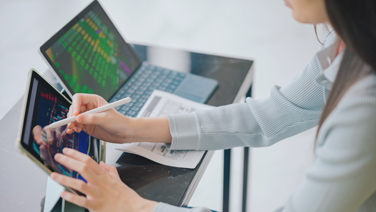 Donna che analizza dati dei mercati finanziari dal tablet con accanto un computer