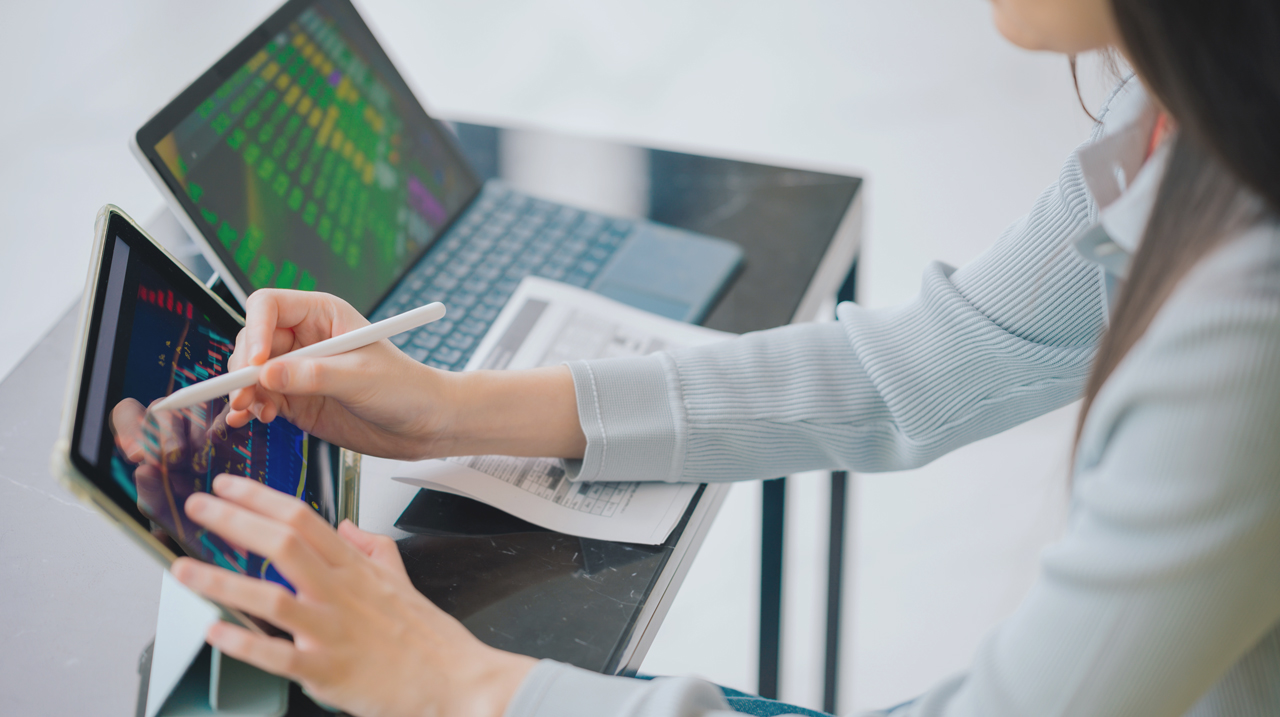 Donna che analizza dati dei mercati finanziari dal tablet con accanto un computer.