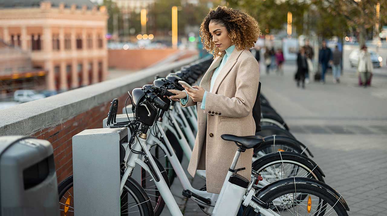 Donna che noleggia una bicicletta elettrica tramite smartphone al parcheggio.