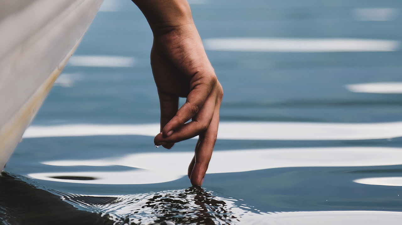 Una mano sfiora l'acqua lasciando la scia