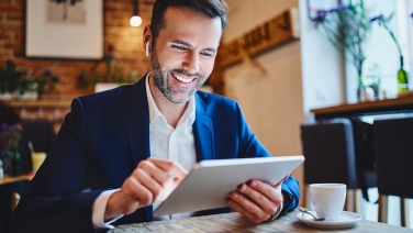 Uomo d'affari seduto al bar consulta il tablet e accede a contenuti multimediali.