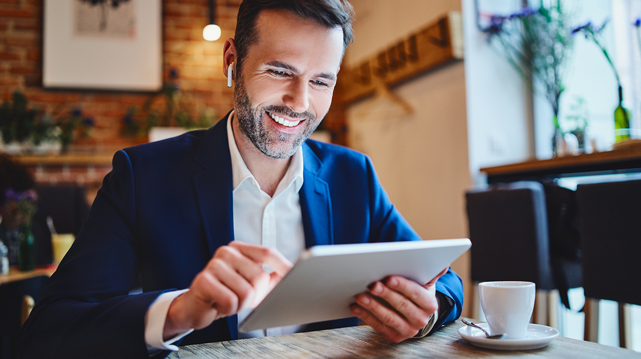 Uomo d'affari seduto al bar consulta il tablet e accede a contenuti multimediali con cuffie wireless