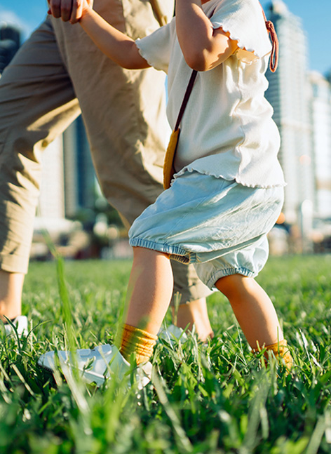 Un adulto e una bambina passeggiano in un prato con una skyline sullo sfondo..