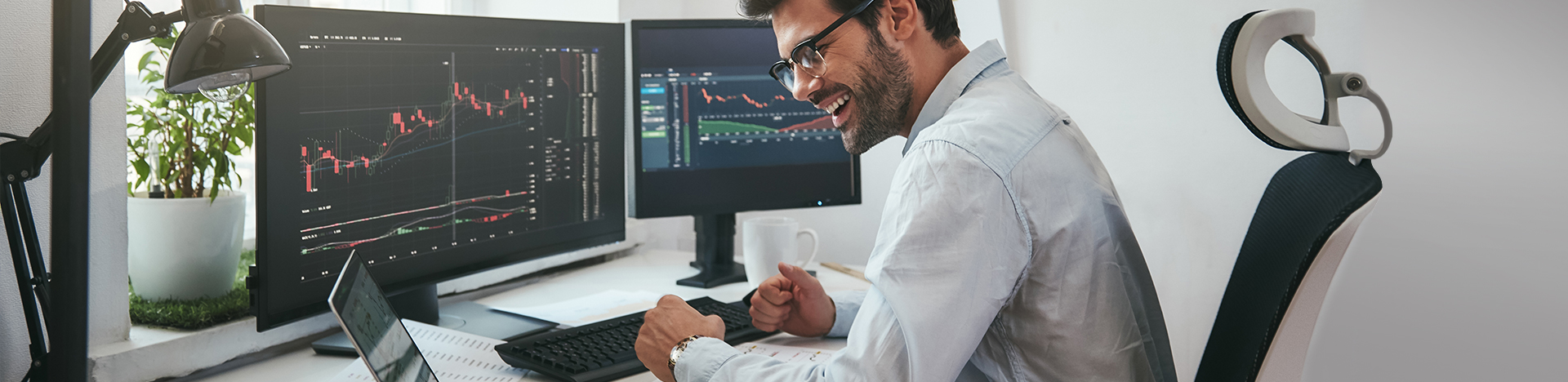 Uomo con tablet e computer, sorride osservando i risultati ottenuti sui mercati finanziari.